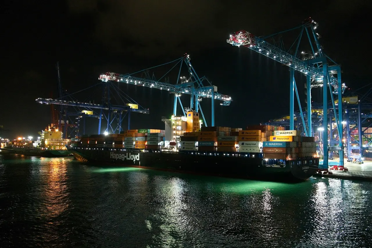 A container ship at a port at night under illuminated cranes